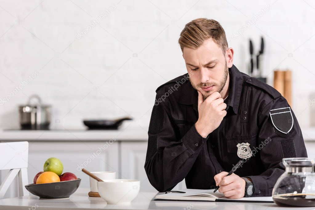 thoughtful policeman writing in notebook at kitchen table