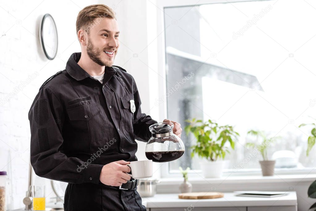 smiling man in police uniform pouring coffee in cup from kettle near kitchen window