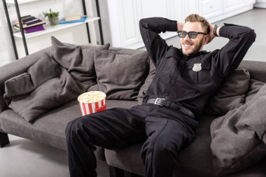 Polis kanepede oturan ve film seyrederken başını elleri ile 3d gözlük