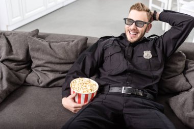 Polis çizgili patlamış mısır kova ve film izlerken kanepede oturan kafasına el ile 3d gözlük gülümseyen