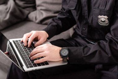 cropped view of policeman typing on laptop keyboard clipart