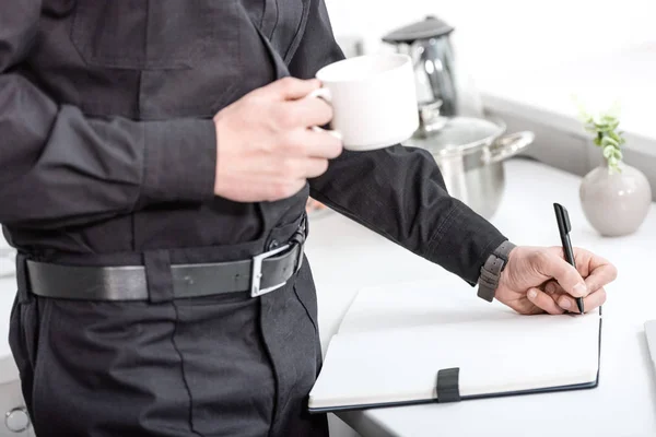 Vista Cortada Policial Segurando Xícara Café Escrevendo Caderno Mesa Cozinha — Fotografia de Stock Grátis