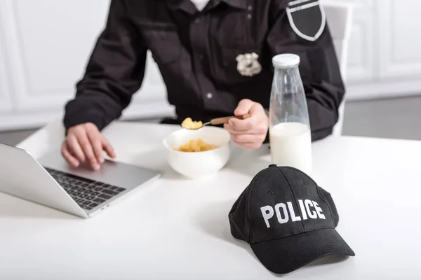 裁剪警察使用笔记本电脑和吃玉米片在厨房桌子上的看法 — 图库照片