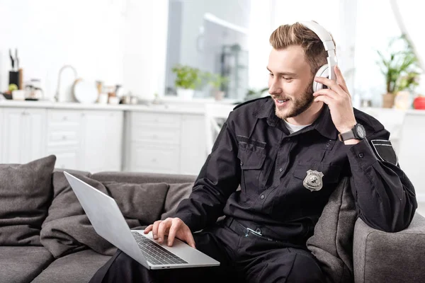 英俊的警察耳机坐在沙发上 使用笔记本电脑 — 图库照片