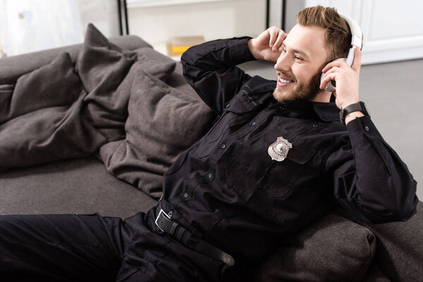 Smiling policeman sitting on couch and putting on headphones