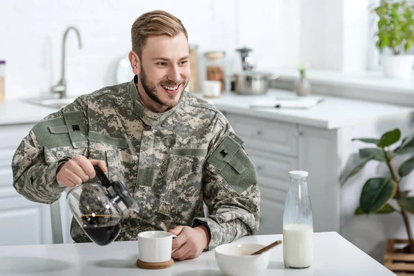Pohledný Muž Vojenské Uniformě Úsměvem Nalití Kávy Šálku Konvice Stole — Stock fotografie zdarma