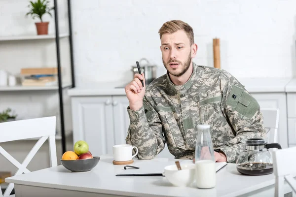 军队士兵坐在厨房的桌子与笔 而吃早餐 — 图库照片