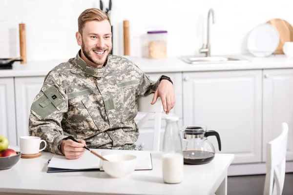 Leende Soldat Sitter Vid Köksbordet Och Äter Frukost — Gratis stockfoto