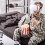 Солдат в наушниках виртуальной реальности, сидит на диване, смотрит кино и ест попкорн