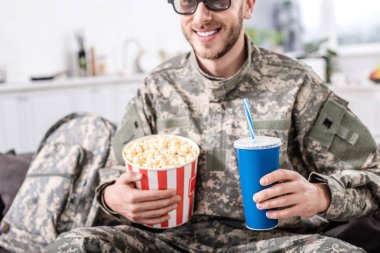 smiling soldier in 3d glasses watching movie with popcorn and soda water  clipart