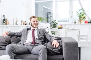 işadamı kulaklıklar giyen ve evde kanepede oturan formal giyim gülümseyen