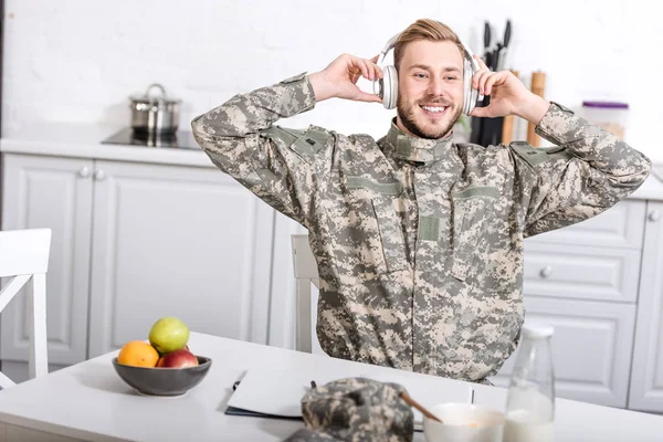 Leende Soldat Hörlurar Som Sitter Vid Köksbordet Frukosten Hemma — Gratis stockfoto