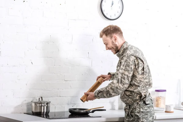 Leende Armésoldat Använder Pepper Pot Medan Matlagning Köket — Gratis stockfoto