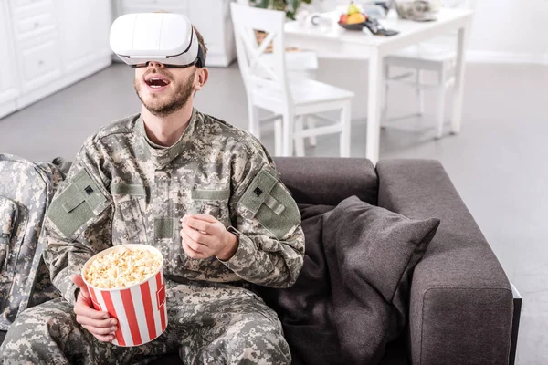 excited soldier in virtual reality headset sitting on couch and eating popcorn