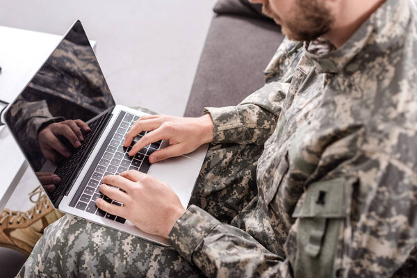 partial view of army soldier using laptop on couch