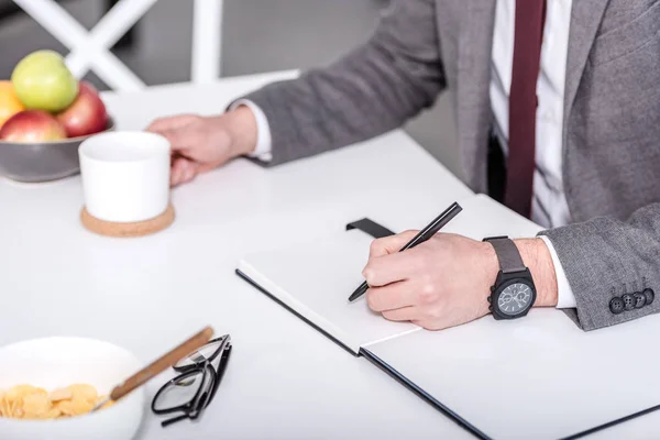 Visão Cortada Empresário Escrevendo Caderno Com Caneta Enquanto Toma Café — Fotografia de Stock