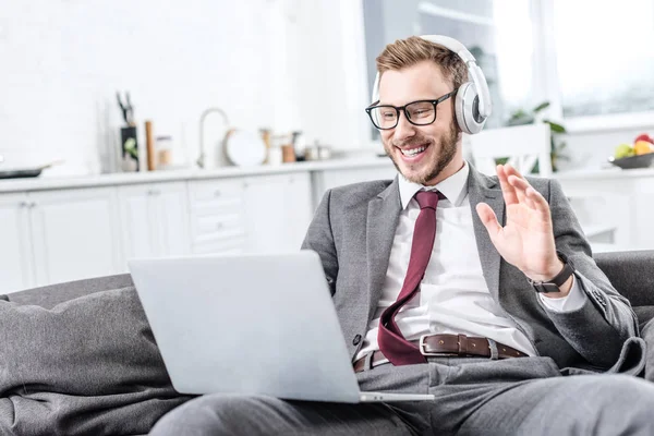 Biznesmen Okularach Noszenia Słuchawek Macha Ręką Pomocą Laptopa Kanapie — Zdjęcie stockowe