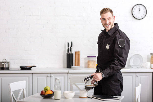 smiling handsome policeman pouring filtered coffee from glass pot at kitchen