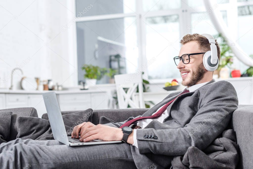 businessman in glasses wearing headphones and using laptop on couch