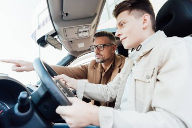 side view of handsome father pointing on something while teaching son driving car clipart