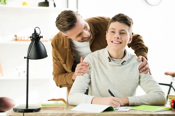 Smiling Father Hugging Happy Teen Son While Doing Homework — Stock Photo, Image
