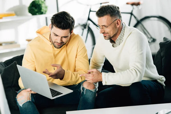 Sohn Zeigt Dem Reifen Vater Etwas Auf Dem Laptop Auf — kostenloses Stockfoto