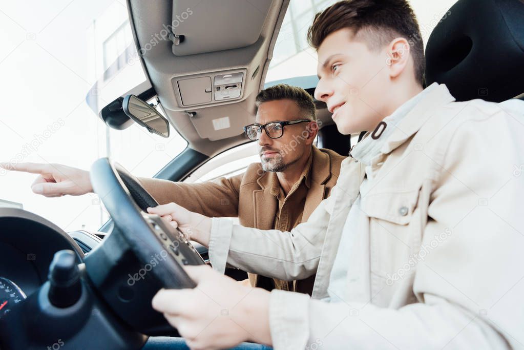 side view of handsome father pointing on something while teaching son driving car