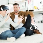 Pai alegre olhando para o filho adolescente assistindo algo com fone de ouvido realidade virtual em casa