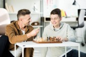 smiling father showing chess figure to teen son while playing chess at home