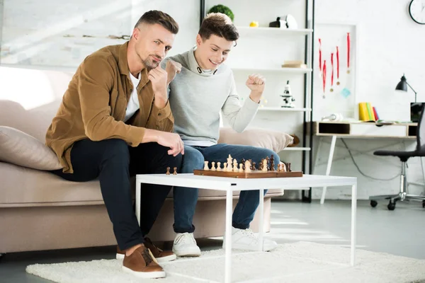 Feliz Hijo Adolescente Ganar Ajedrez Mientras Juega Con Padre Casa — Foto de stock gratuita