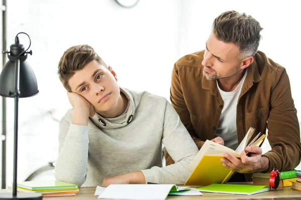 Father Holding Book Pensive Teen Son Looking Away Home — Stock Photo, Image