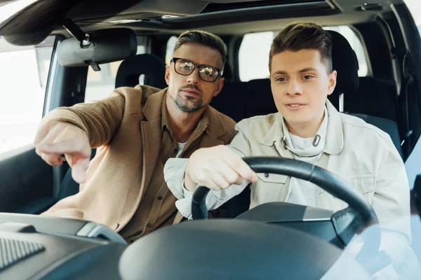 Schöner Vater Zeigt Auf Etwas Während Teenager Sohn Autofahren Beibringt — Stockfoto