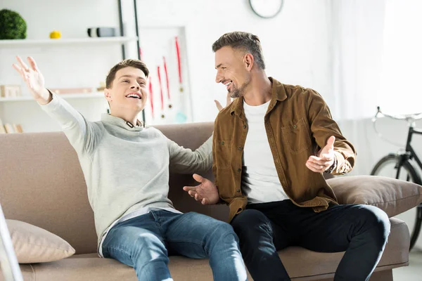 Sorrindo Pai Filho Adolescente Sentado Sofá Gesticulando Olhando Para Outro — Fotografia de Stock