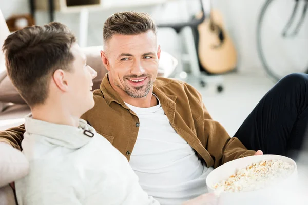 Uśmiechnięty Ojciec Syn Nastolatka Oglądania Telewizji Trzymając Miskę Popcornem Razem — Zdjęcie stockowe