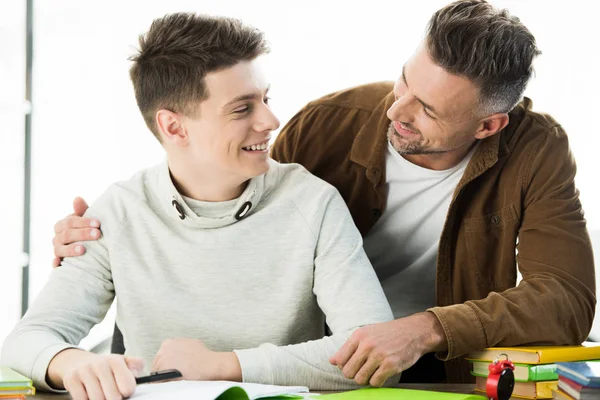 Sonriente Padre Abrazando Adolescente Hijo Mientras Haciendo Tarea Mirándose Uno — Foto de Stock