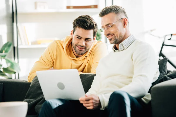 Son Looking Cheerful Mature Father Using Laptop Sofa Home — Stock Photo, Image