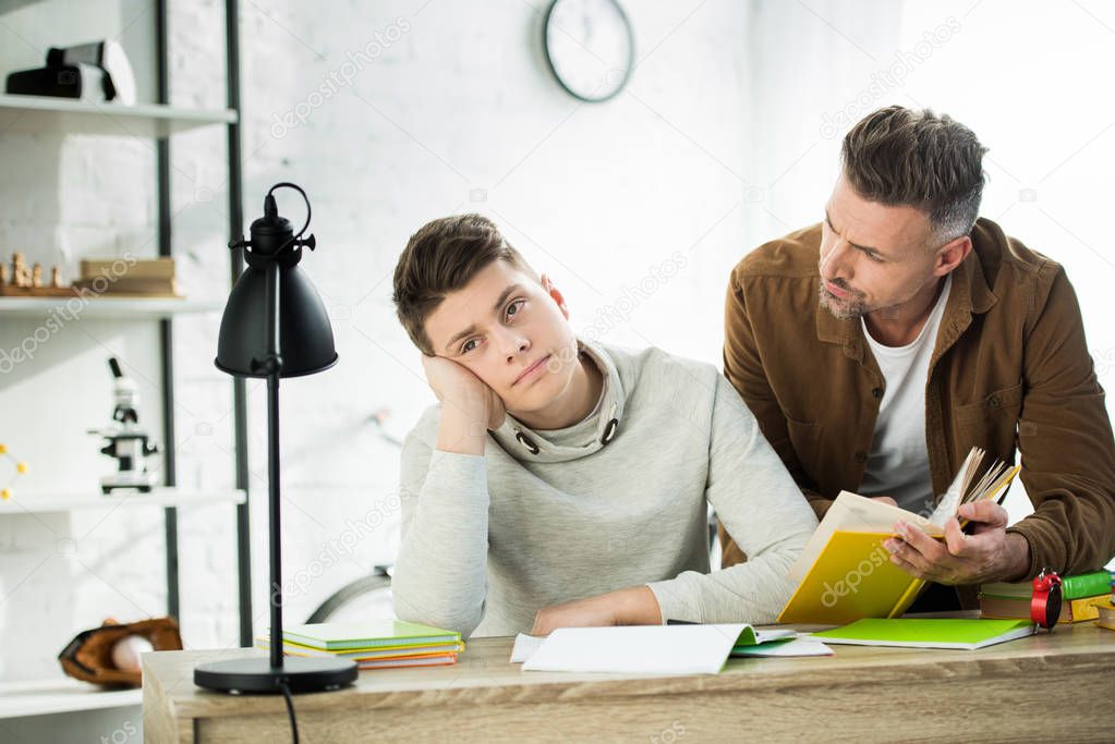 father holding book, pensive teen son looking away 