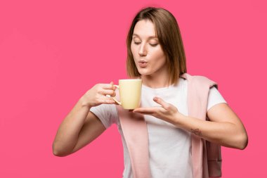 Kupası tutarak ve sıcak içecek pink izole üzerinde üfleme genç kadın