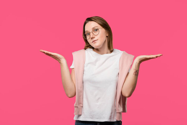 stylish woman in eyeglasses doing shrug gesture isolated on pink