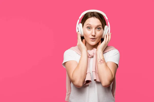 ピンクの分離された音楽を聴くヘッドフォンに驚いた若い女性  — 無料ストックフォト