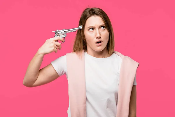 Молода Жінка Тримає Револьвер Біля Голови Дивиться Ізольовано Рожевий — Безкоштовне стокове фото