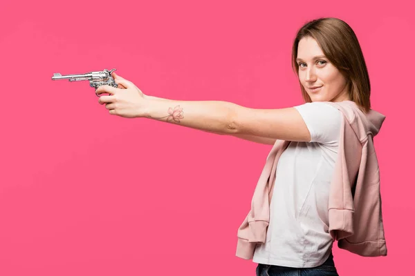 Вид Збоку Молода Жінка Тримає Револьвер Посміхається Камеру Ізольовано Рожевому — Безкоштовне стокове фото