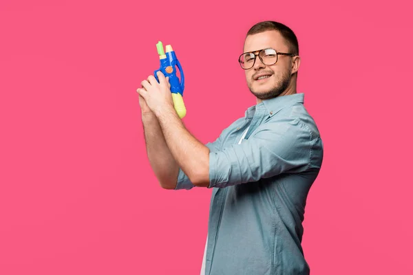 Молодий Чоловік Окулярах Тримає Іграшковий Пістолет Посміхається Камеру Ізольовано Рожевому — стокове фото