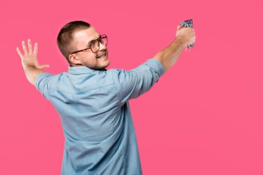 back view of smiling man in eyeglasses holding staple gun and looking at camera isolated on pink clipart