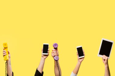 cropped shot of hands holding smartphones, digital tablet and handsets isolated on yellow 