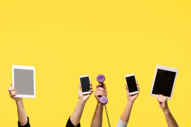 cropped shot of hands holding smartphones, digital tablets and handset isolated on yellow  clipart