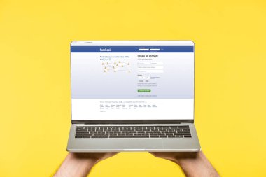 Web sitesi facebook ile dizüstü bilgisayar ekranında sarı izole tutan kişi kırpılmış atış