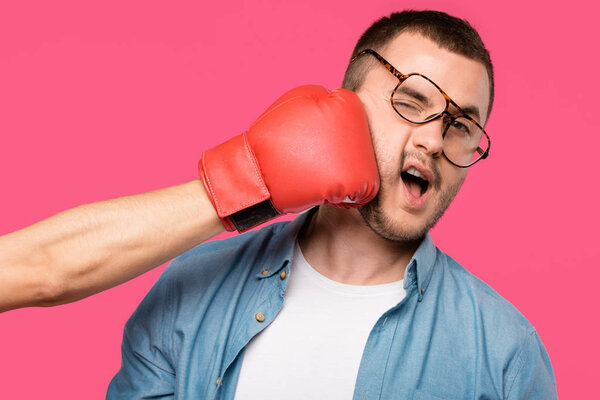 cropped shot of someone in boxing glove hitting man in eyeglasses isolated on pink