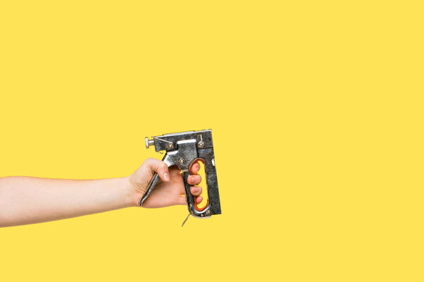 Cropped shot of person holding powered stapler isolated on yellow