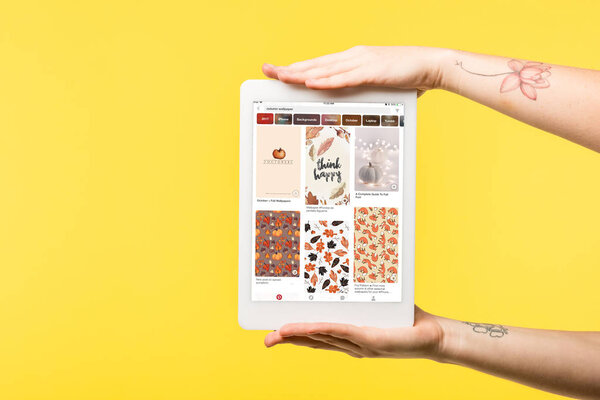 cropped shot of person holding digital tablet with pinterest app isolated on yellow